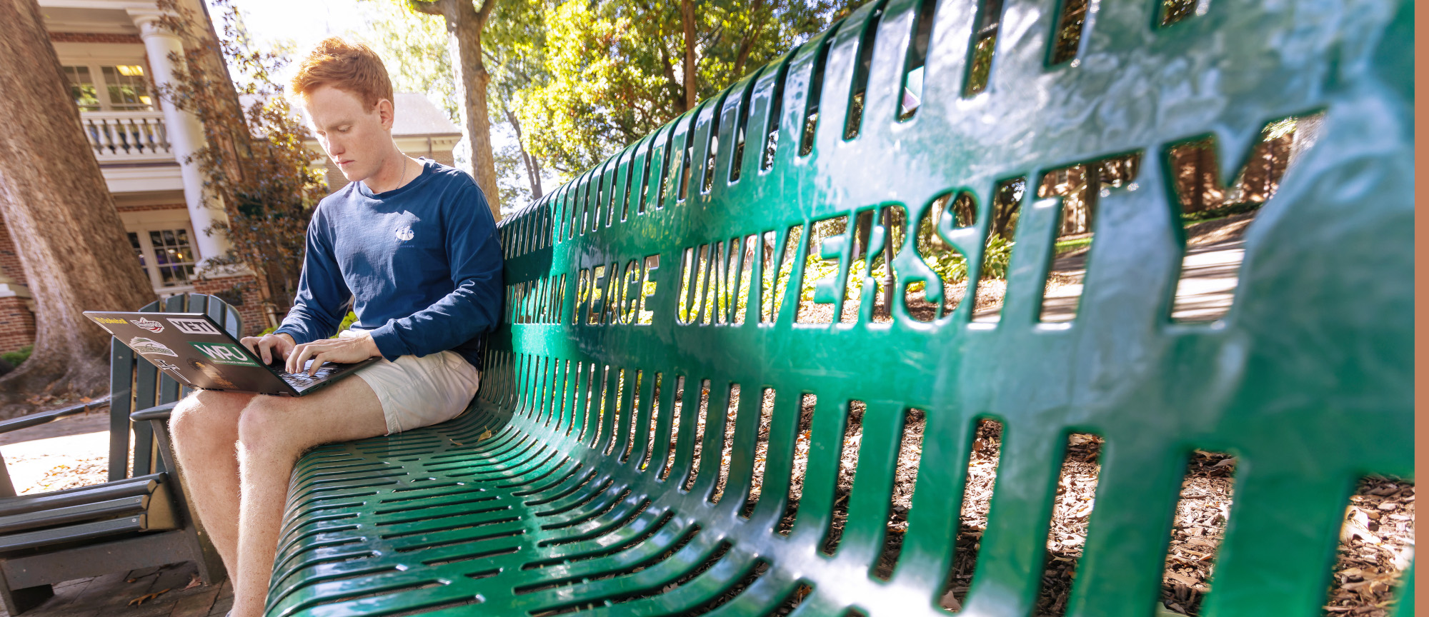 a student uses a laptop on a green bench at William Peace University